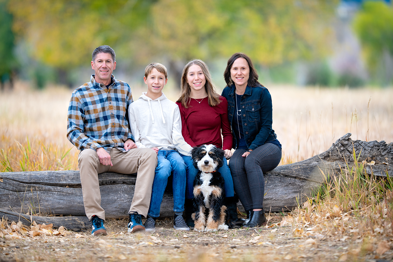 A family of four sitting on a log with their dog.