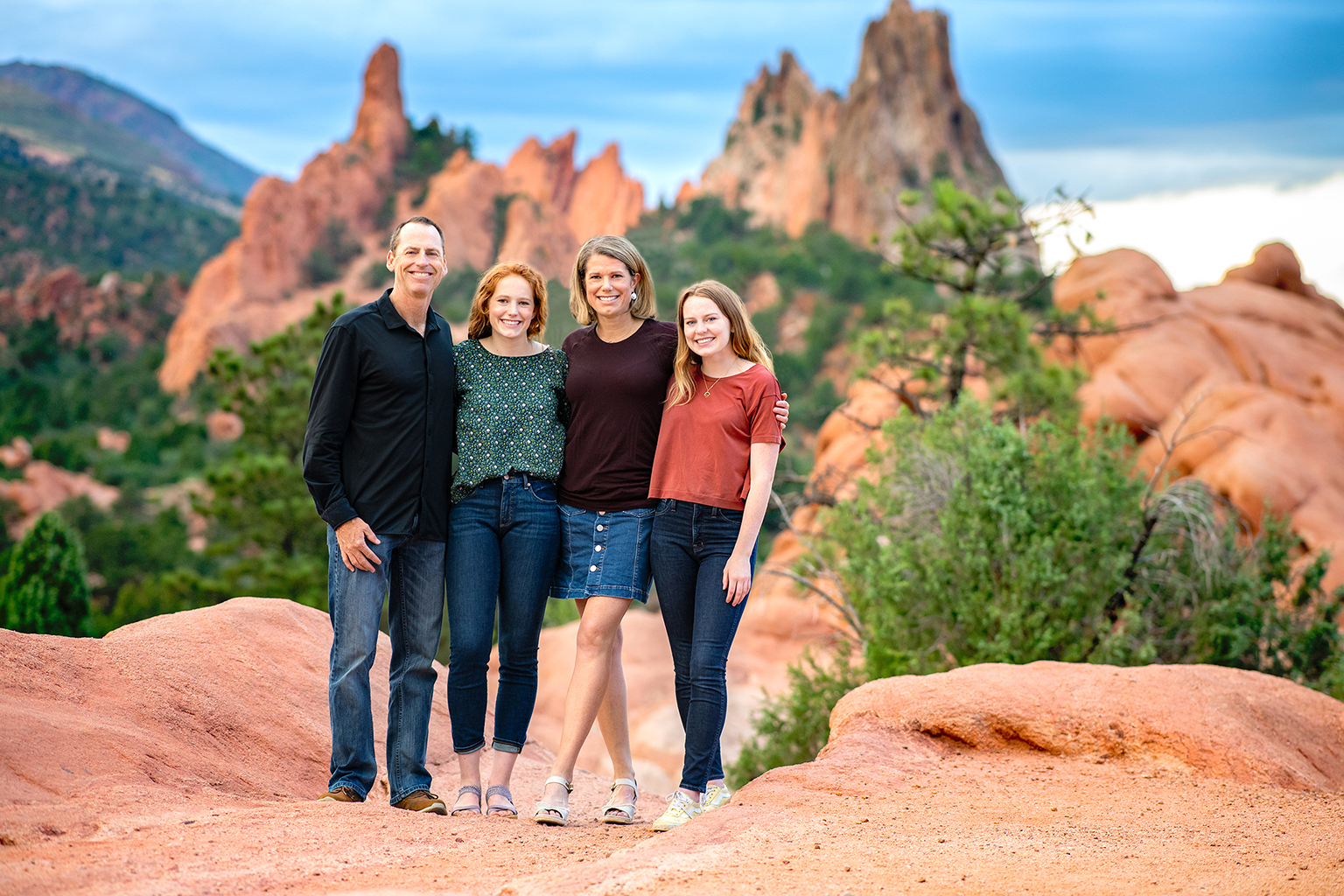 A family of four standing on top of red rocks.
