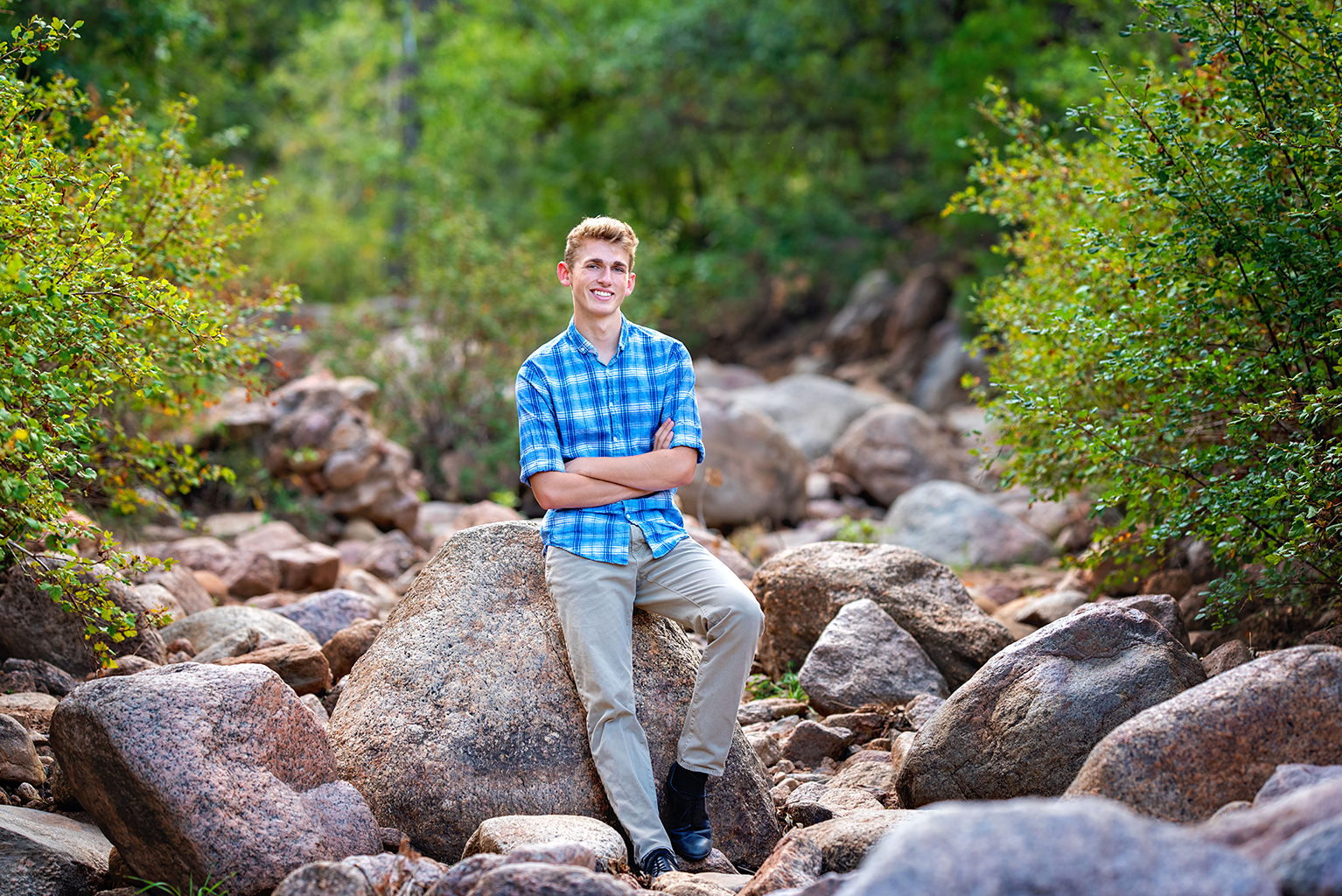 A young man wearing a plaid shirt leaning against a rock.