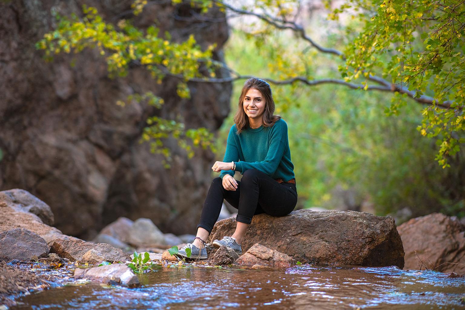 A young woman sitting on a rock in the middle of a stream.