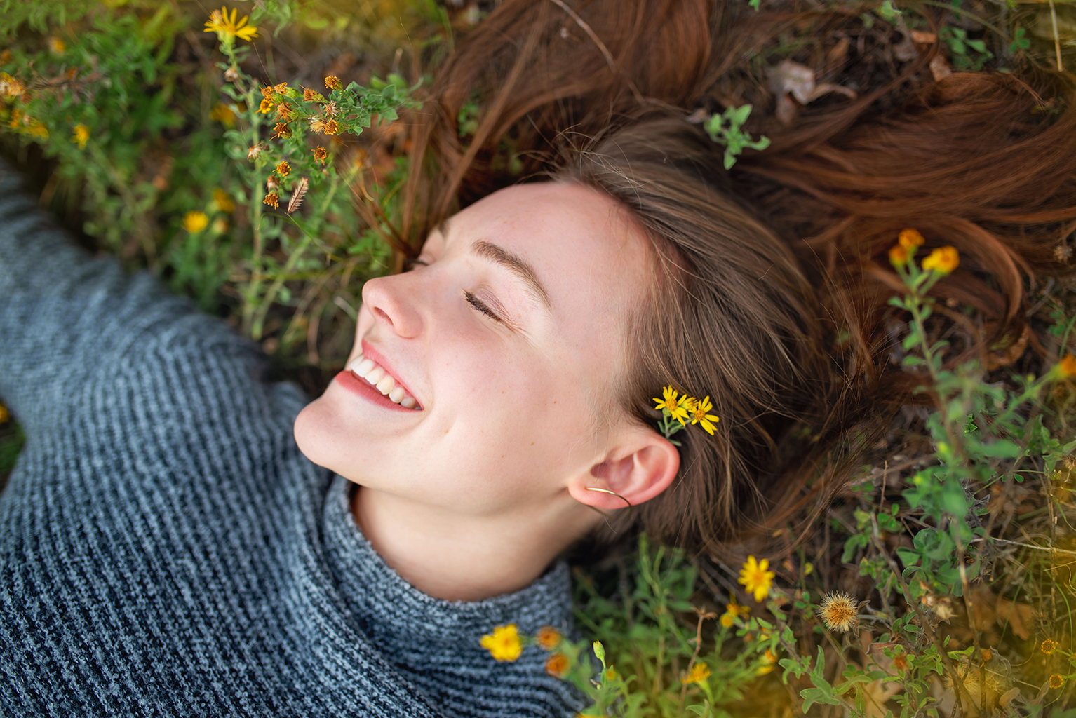 A young women laying down in a grass with flowers.