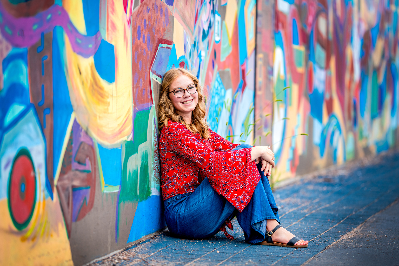 A young woman sitting against a graffiti wall.